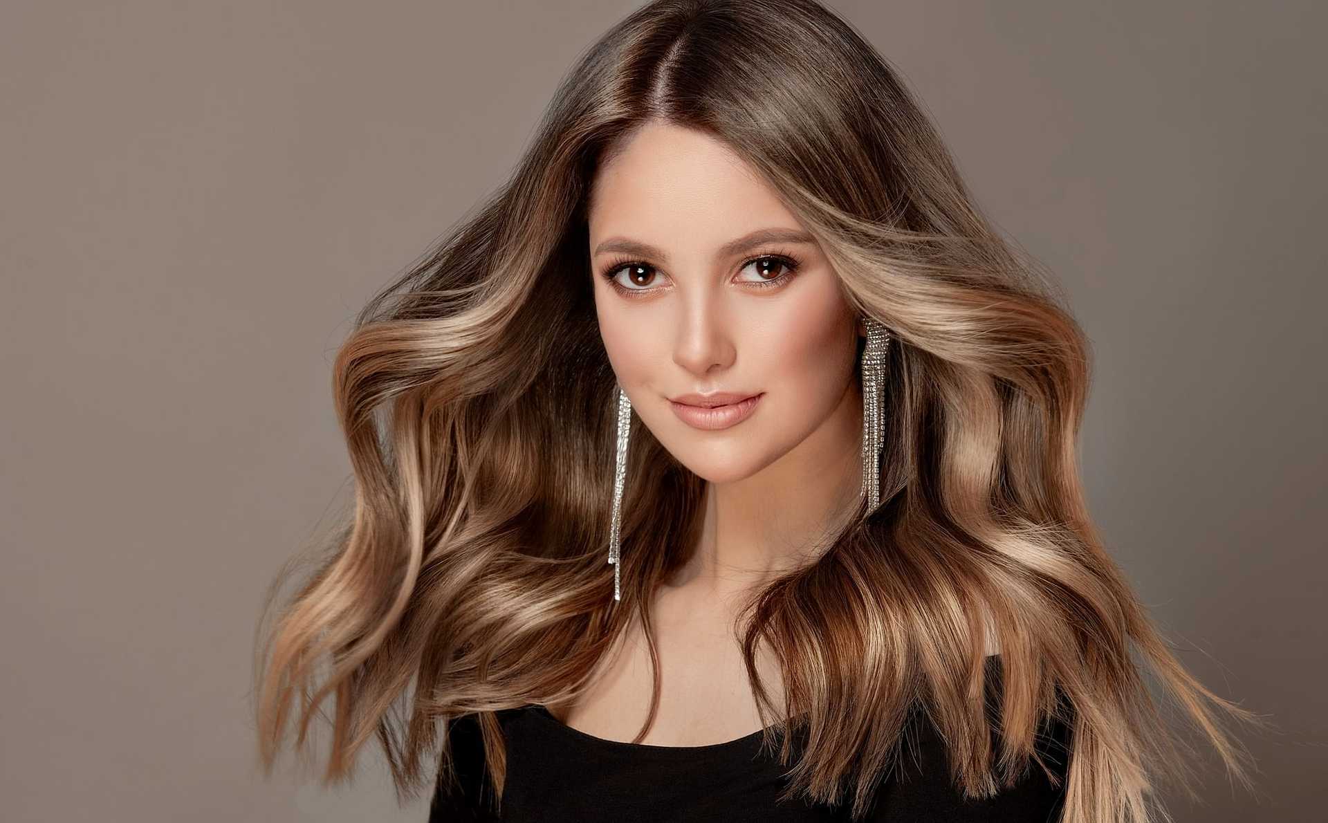 Elegant woman with flowing hair and long earrings, wearing a black top.