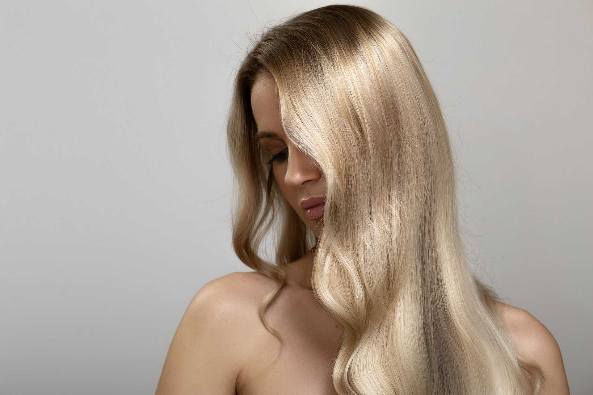 Woman with long, blonde hair looking down against a plain background.